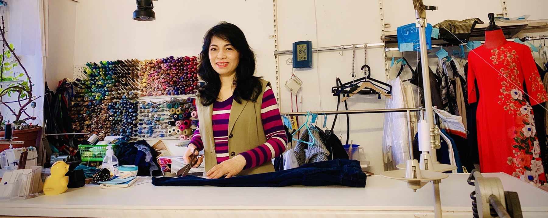 Die Inhaberin Pham
      sitzt in ihrem Laden vor einem Kleidungsstück, das sie gerade
      bearbeitet